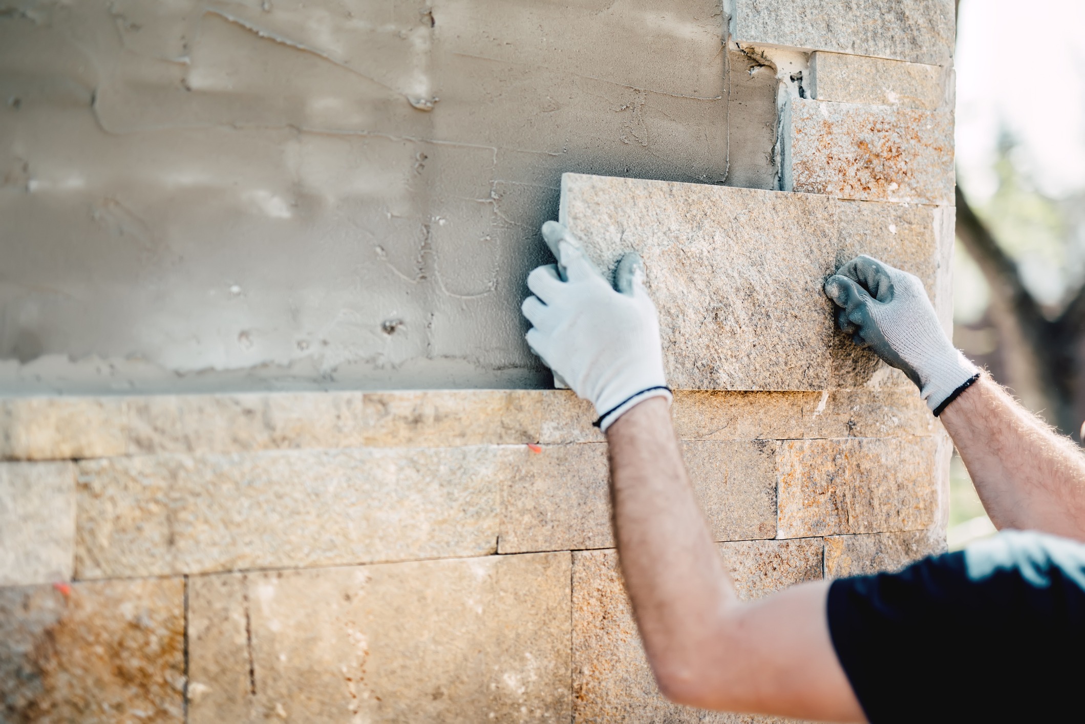 A skilled landscape technician installs stone on an architectural facade.