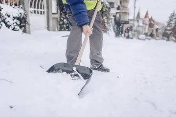 A landscape technician shovels snow outside a business.